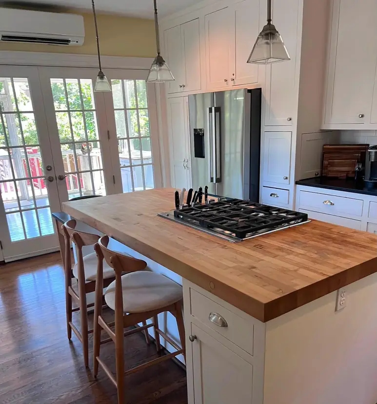 A bright kitchen after a clean: butcher-block island, gas cooktop, white shaker cabinets and French doors to the deck